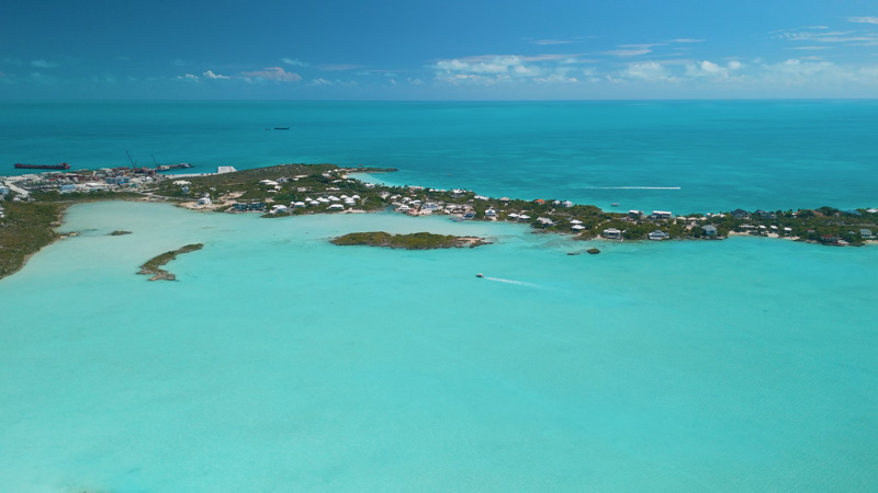 Aerial view of small boat moving within Chalk Sound with villas in the background