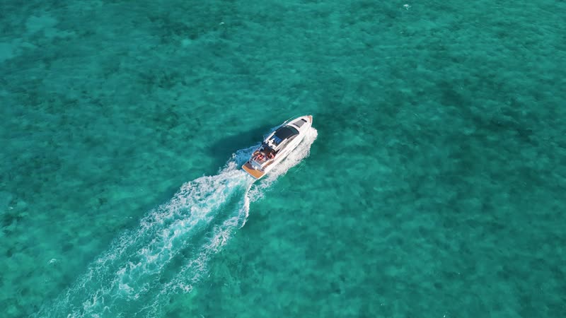 Dynamic drone shot of luxury yacht cruising through clear Grace Bay waters