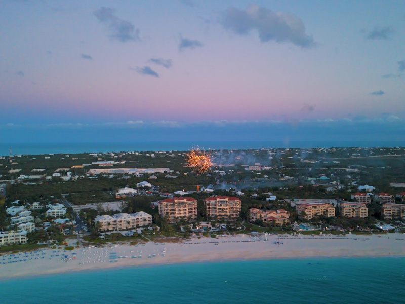 Drone pan around fireworks display behind beachfront resorts at sunset