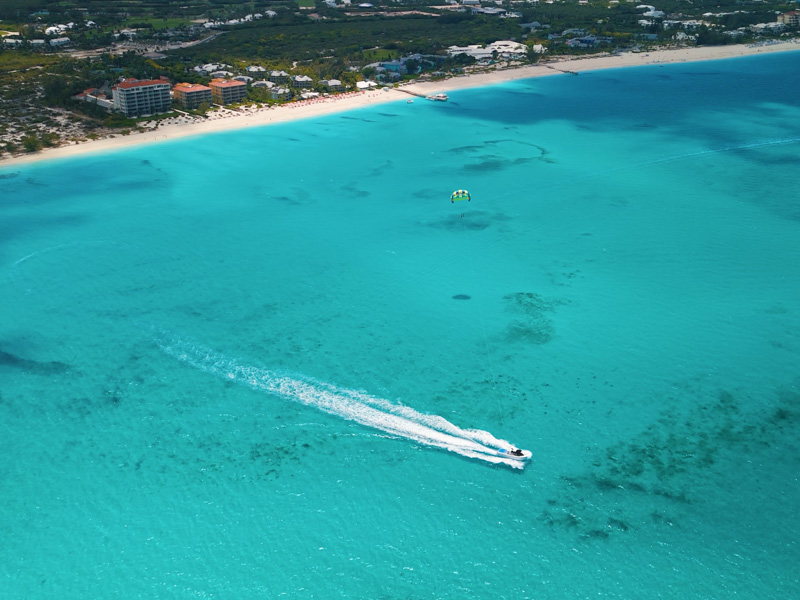 Drone pan around parasailing boat and canopy over turquoise water
