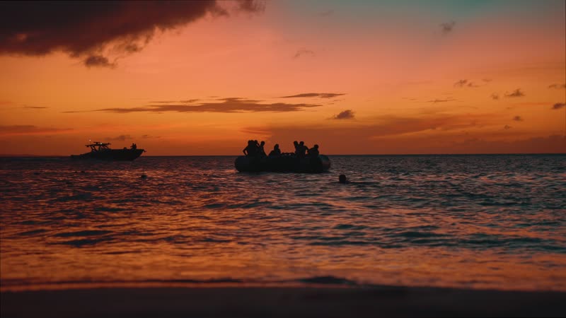 Handheld camera shot of tourists playing on water trampoline along Grace Bay Beach during sunset