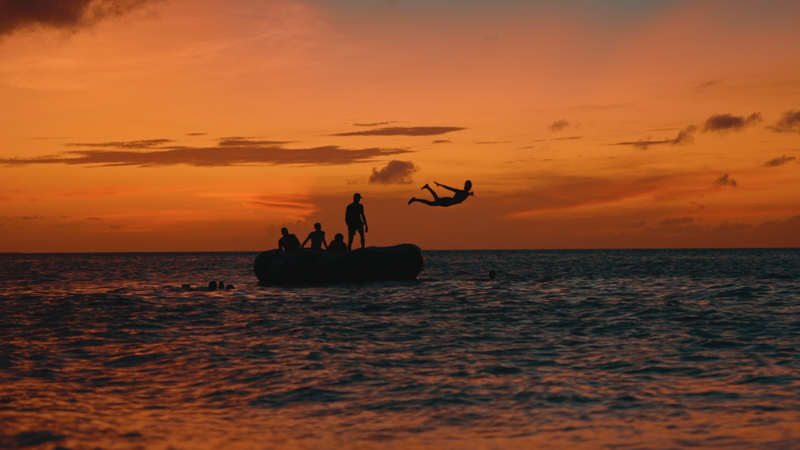 Handheld camera shot of tourists playing on water trampoline along Grace Bay Beach during sunset