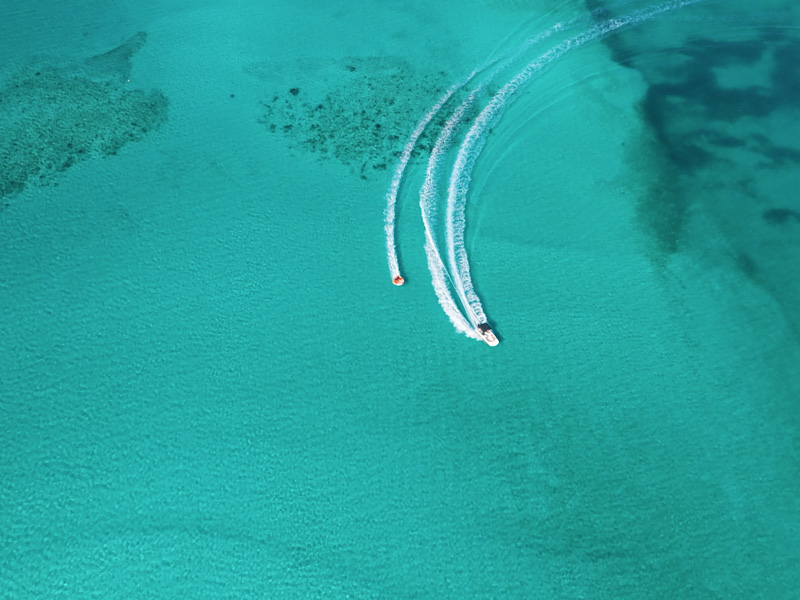 Drone aerial of tubing behind speedboat in clear turquoise water