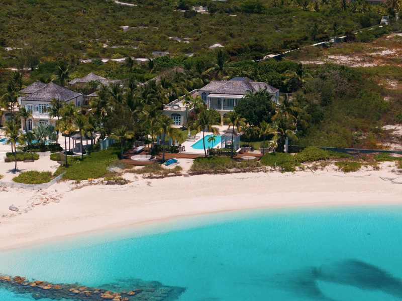 Drone shot of beachfront luxury villas with pools and palm trees