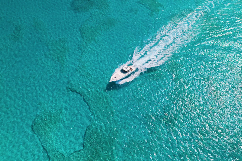 Drone shot of luxury yacht cruising through shallow turquoise water