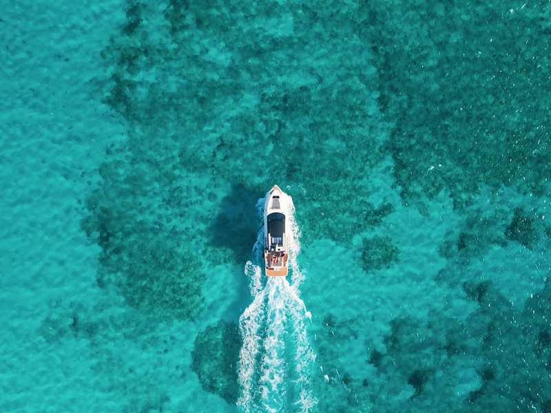 Drone shot tracking a yacht cruising over clear reef