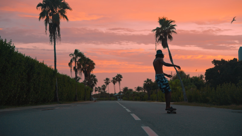 Low shot of tourist skateboarding through Leeward during sunset