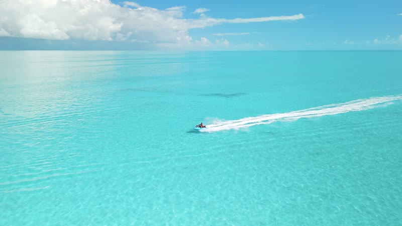 Drone shot of jetski moving through glass-like Long Bay water